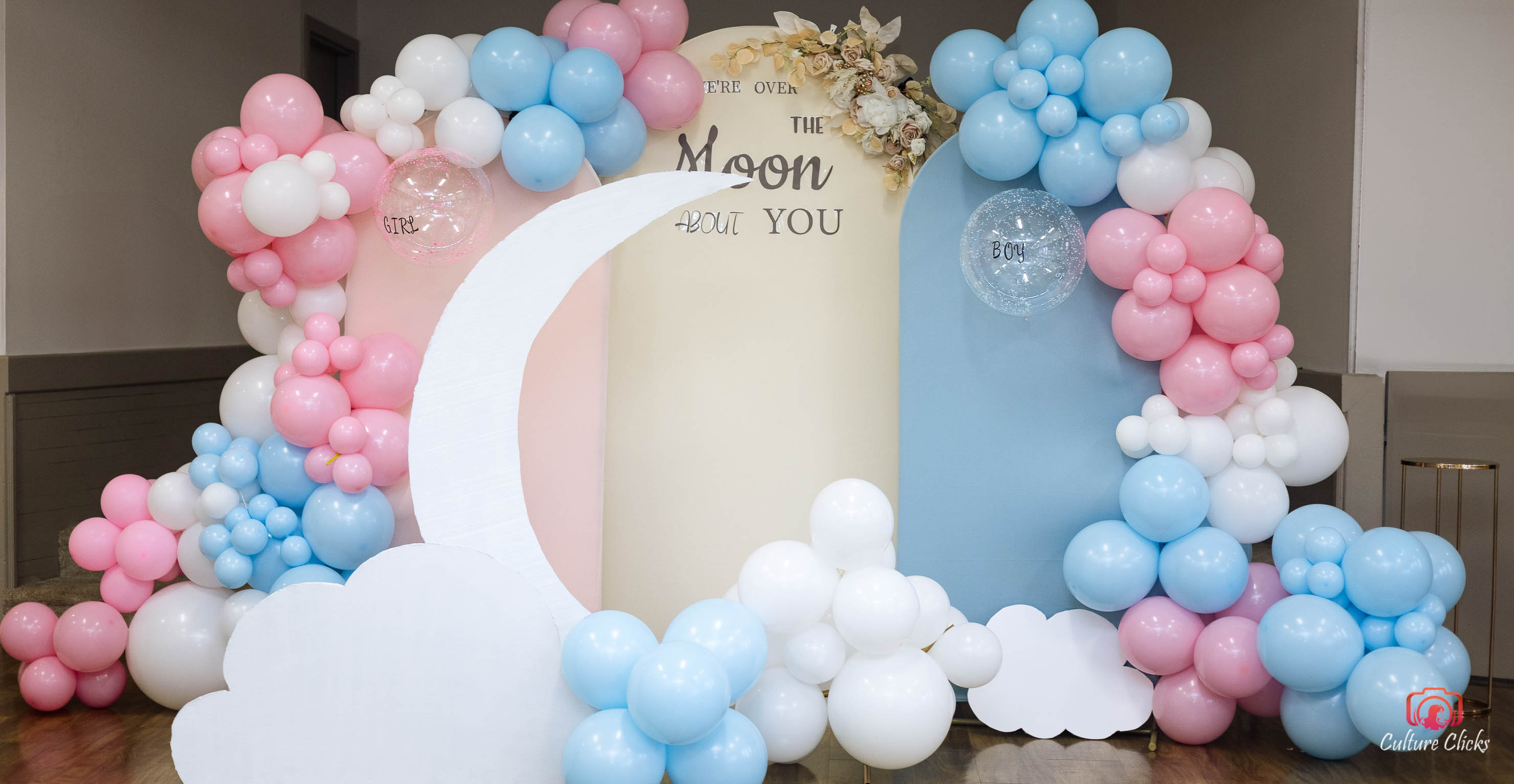 Gender reveal baby shower decorations with pink and blue balloons, crescent moon, and 'Over the Moon About You' backdrop done by Culture Clicks party Decor