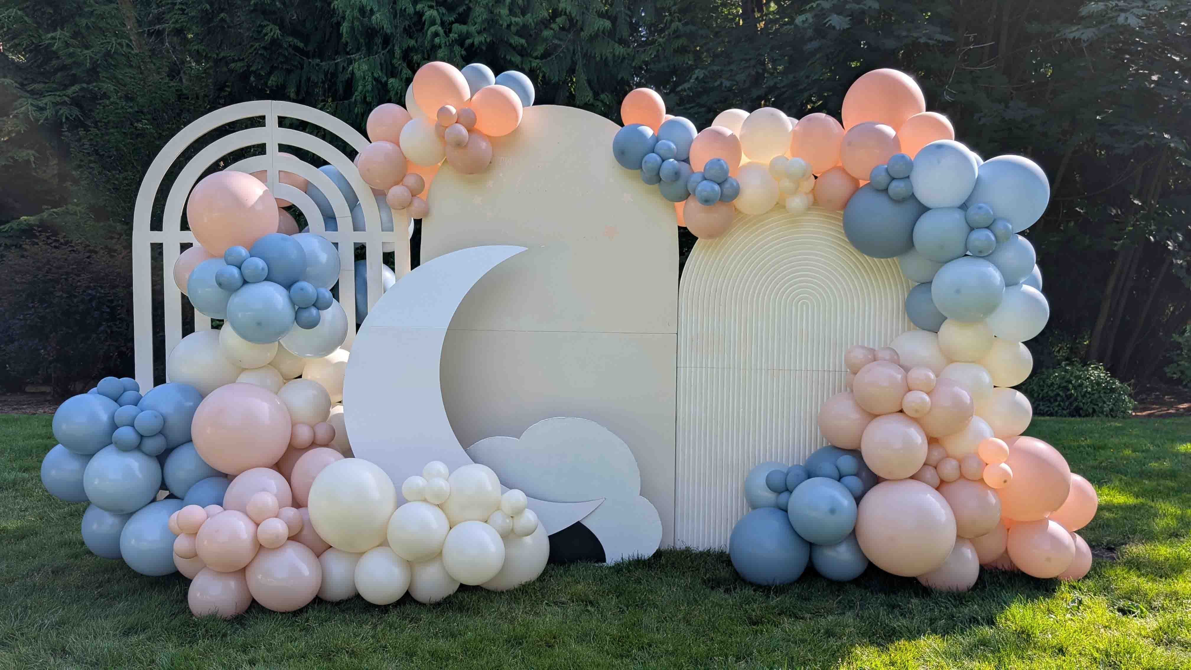 Pastel moon and cloud balloon backdrop in a garden for a gender reveal