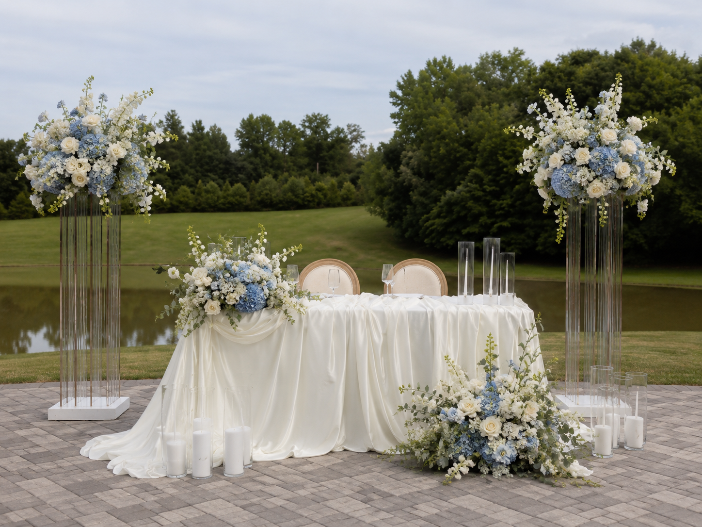 Ivory sweetheart table with tall blue and white floral arrangements by a lake